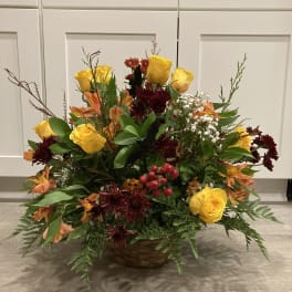 Basket arrangement of yellow roses and orange flowers with burgundy blooms