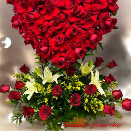 Heart-shaped red rose display with tiara above a base of red roses, white lilies, and yellow filler flowers.