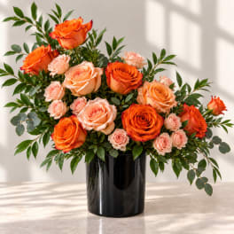 Orange and peach roses in a black vase with greenery