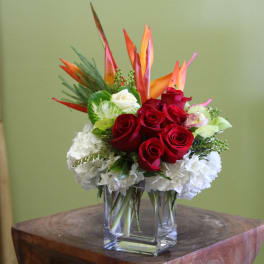 Red roses and white hydrangeas in a clear glass vase with orange tropical blooms