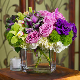 Pink and purple bouquet in a square glass vase with a candle nearby