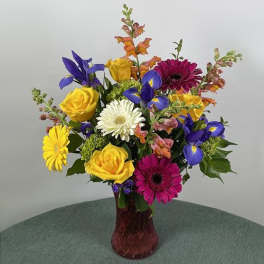 Mixed bouquet of roses, gerbera daisies, irises, and snapdragons in a red vase