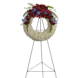 Circular funeral wreath of red and white flowers on a metal stand