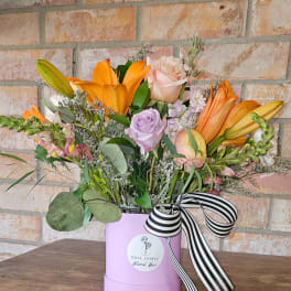 Mixed arrangement of orange lilies and pastel roses in a lavender hatbox with striped ribbon
