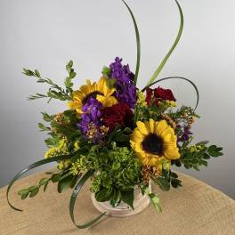 Bouquet of sunflowers, red roses, and purple flowers in a white basket