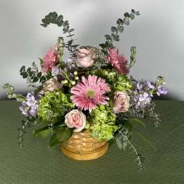 Pink gerbera daisies and roses in a woven basket with lavender accents