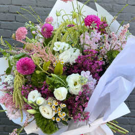 Hand-tied bouquet of pink, white, and purple flowers wrapped in white paper