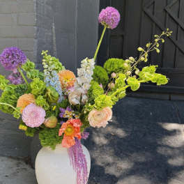 Large mixed floral arrangement in a white vase with purple, peach, and green blooms