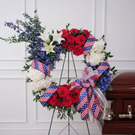 Red, white, and blue floral wreath on a stand with ribbon bows