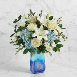 White lilies and roses with blue hydrangeas in a blue glass vase