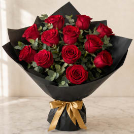 Bouquet of red roses wrapped in black paper with a gold ribbon
