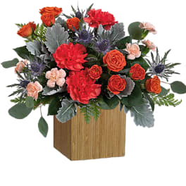 Orange and red roses with carnations in a wooden cube vase