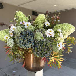 Large floral arrangement with green hydrangeas, white daisies, and a copper vase