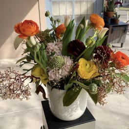 Mixed bouquet of orange, yellow, and burgundy flowers in a white vase