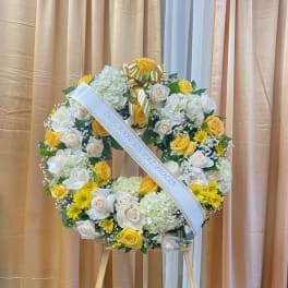 White and yellow floral wreath on a stand with a ribbon