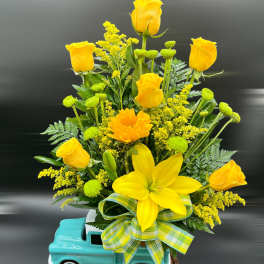 Yellow roses and a lily arranged in a turquoise truck planter