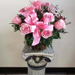Pink rose bouquet with a ribbon in a glass vase on a decorative pedestal