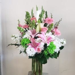 Pink lilies and white flowers arranged in a glass vase on a pedestal