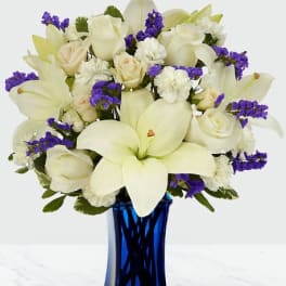 White lilies and roses with purple filler in a blue vase