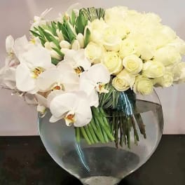 White orchids and pale roses arranged in a clear round vase