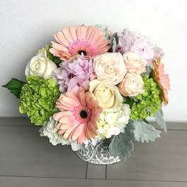 Bouquet of pink gerbera daisies, cream roses, and green hydrangeas in a patterned vase
