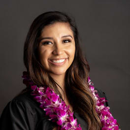Woman wearing a purple orchid lei over a black graduation gown