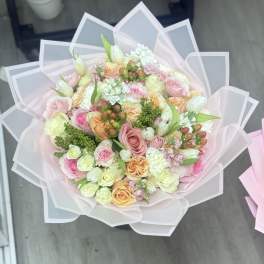 Pastel bouquet of roses and mixed blooms wrapped in translucent pink paper