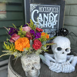 Colorful bouquet in a skull-shaped vase beside a decorative skull