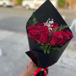 Handheld bouquet of red roses with white filler flowers wrapped in black paper and red ribbon