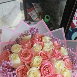 Round bouquet of pink and cream roses with lavender filler flowers wrapped in pink translucent paper