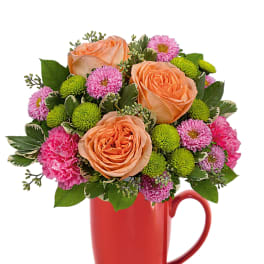 Peach roses and pink flowers arranged in a red mug