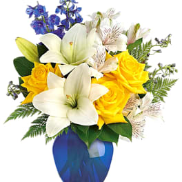 Yellow roses and white lilies in a blue vase with blue flowers