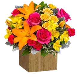 Bright mixed bouquet in a wooden cube vase with roses and lilies