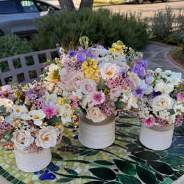 Three pastel floral centerpieces in white ceramic vases on a mosaic table