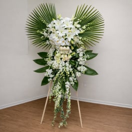 Tall white floral standing spray with palm fronds on an easel