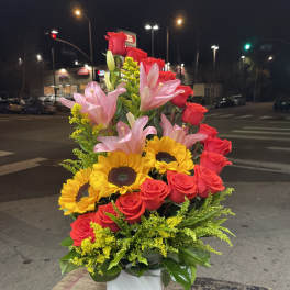 Bouquet of red roses, pink lilies, and sunflowers in a white vase