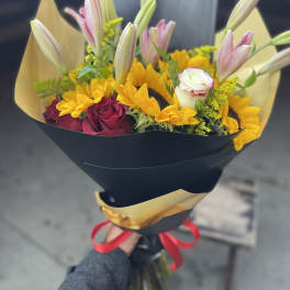 Bouquet of pink lilies, yellow sunflowers, and red roses wrapped in black paper