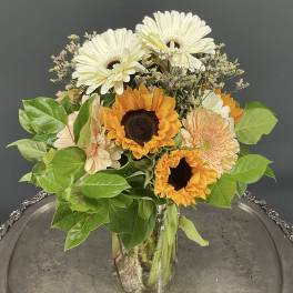 Sunflowers and pale gerbera daisies in a clear glass vase