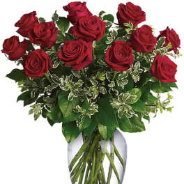 Red roses arranged in a clear glass vase with mixed greenery