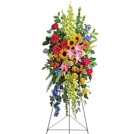 Tall standing floral spray with roses, lilies, sunflowers, and blue accents