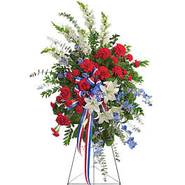 Standing floral spray with red carnations, white lilies, and blue accents on an easel
