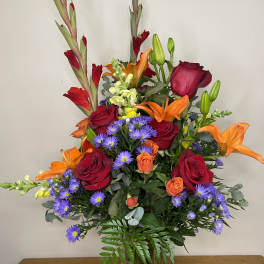 Mixed bouquet of red roses, orange lilies, and purple daisies in a clear vase