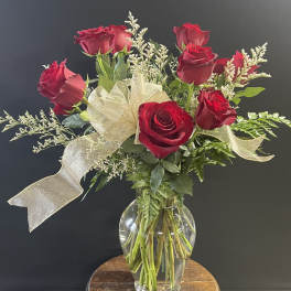 Red roses arranged in a clear glass vase with a gold ribbon