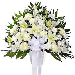 White funeral spray with lilies, roses, and a ribbon on a stand