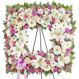 Large floral wreath on a black stand with white lilies, daisies, and pink blooms