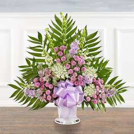 Standing floral spray with pink and lavender blooms in a white vase with a purple bow