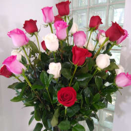 Tall arrangement of red, pink, and white roses in a clear glass vase