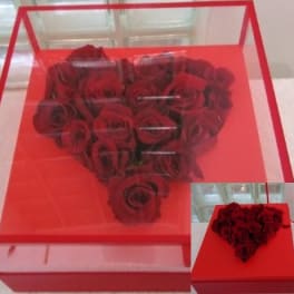 Heart-shaped arrangement of red roses in a clear box with a red base