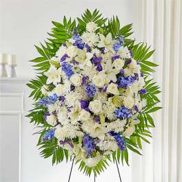 Large standing floral spray with white and blue flowers on a green palm backdrop