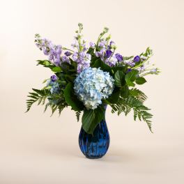 Blue hydrangeas and purple flowers in a blue glass vase